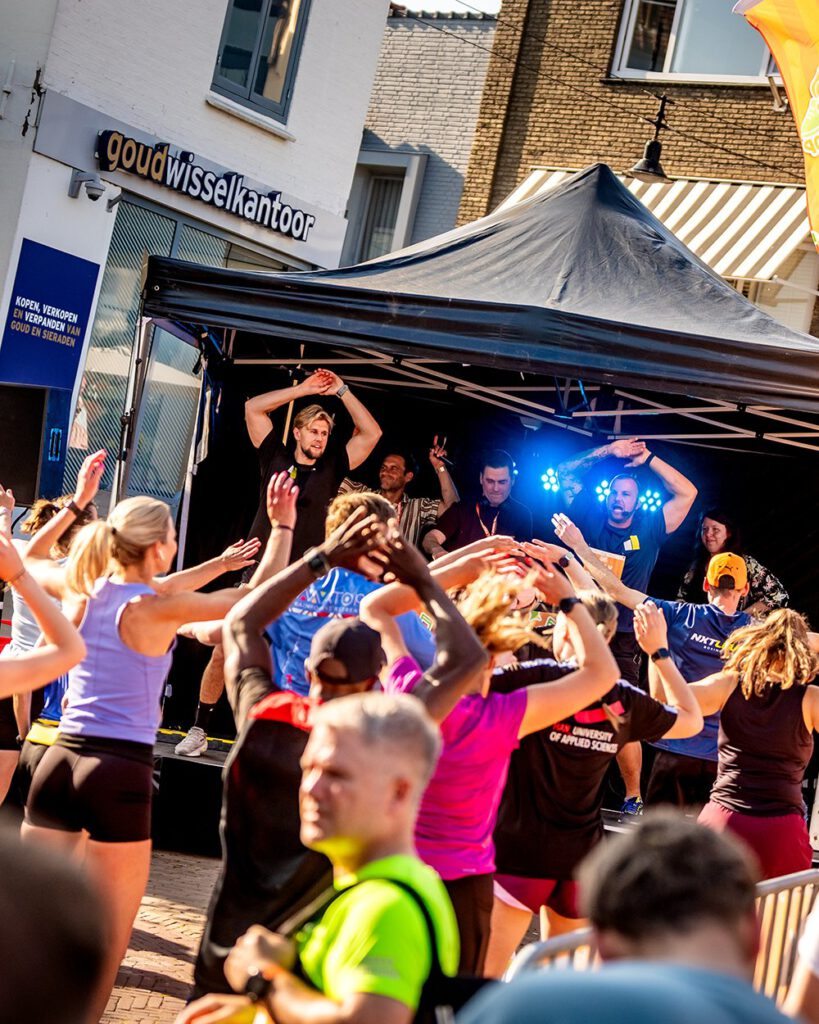 Publiek en lopers dansen met de handen in de lucht bij het muziekpodium