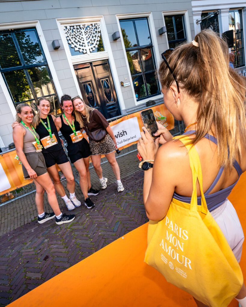 Vier finishers met medaille poseren voor een foto op de oranje finishloper