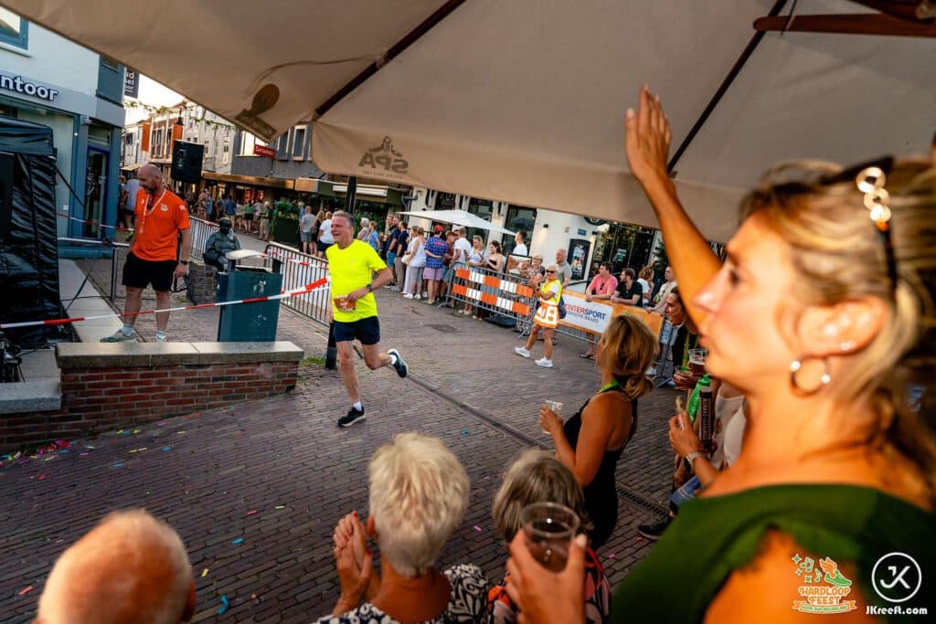 Toeschouwers onder een parasol juichen een passerende loper toe