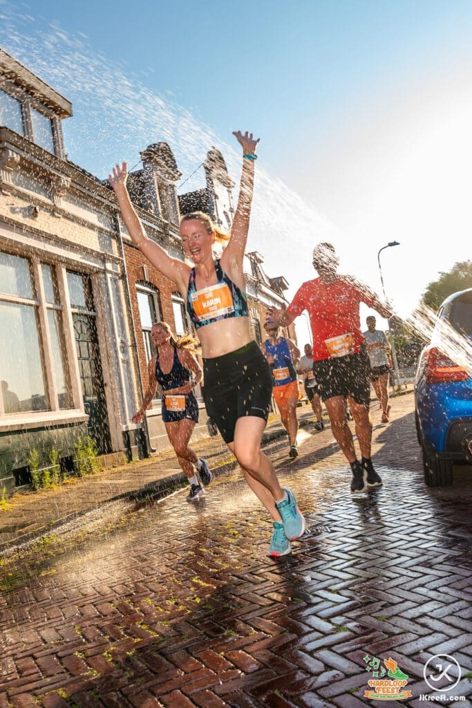 Loopster juicht met de armen omhoog onder een waterstraal