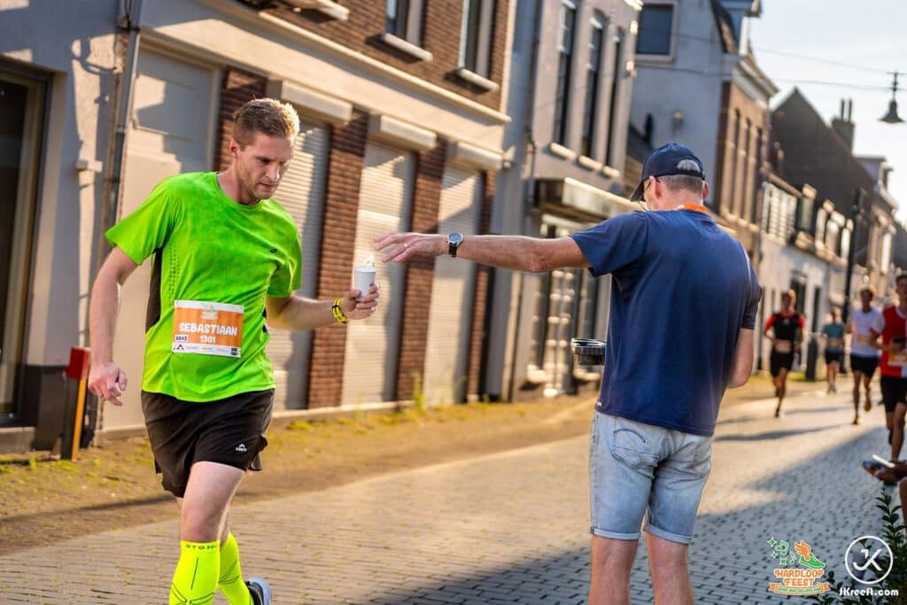 Toeschouwer reikt een loper een bekertje water aan