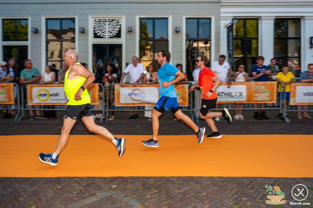 Drie lopers op de oranje finishloper langs de sponsorborden