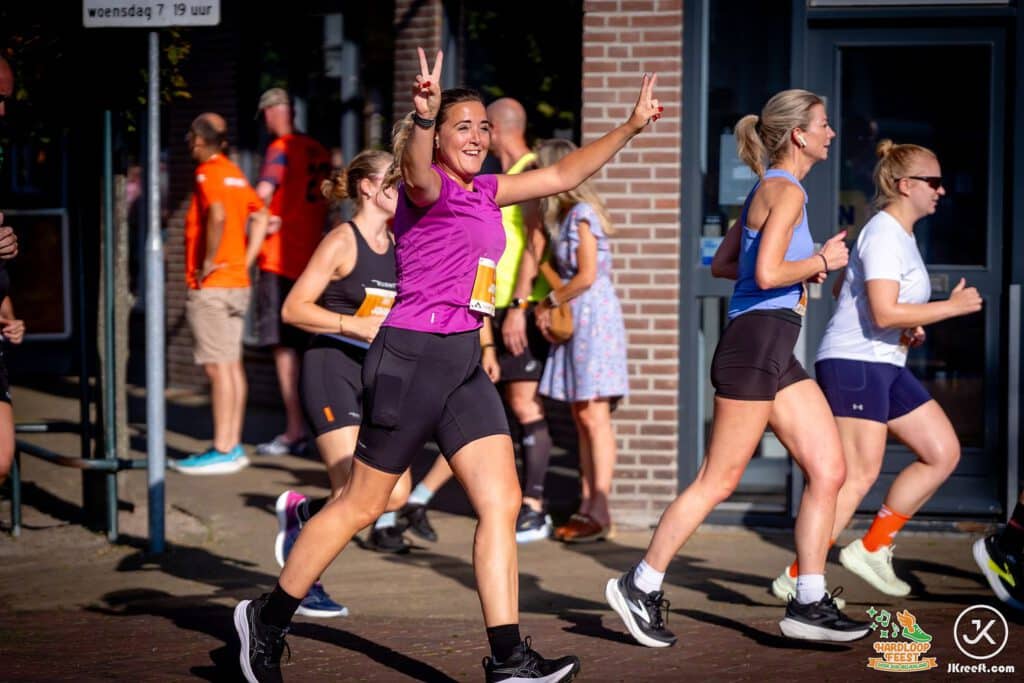 Lachende loopster steekt twee vingers op tijdens de start